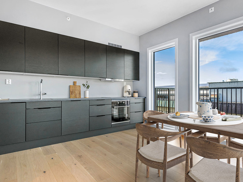 Bildet viser en stue i boligprosjektet Wessel Park i Vestby. Det er parkett på gulvet, grått teppe en lys grå sofa og en grønn plante i høyre hjørne. Et fargerikt maleri henger på veggen og store vinduer gir mye lys inn i leiligheten.