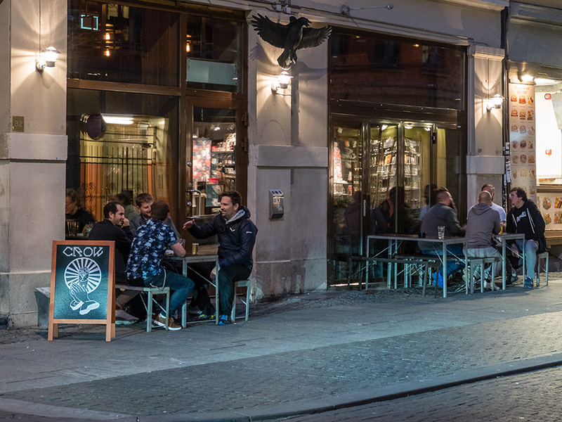 Bildet viser fasaden på Crowbar i Oslo. Murbygning med stoler og bord utenfor hvor mennesker hygger seg.