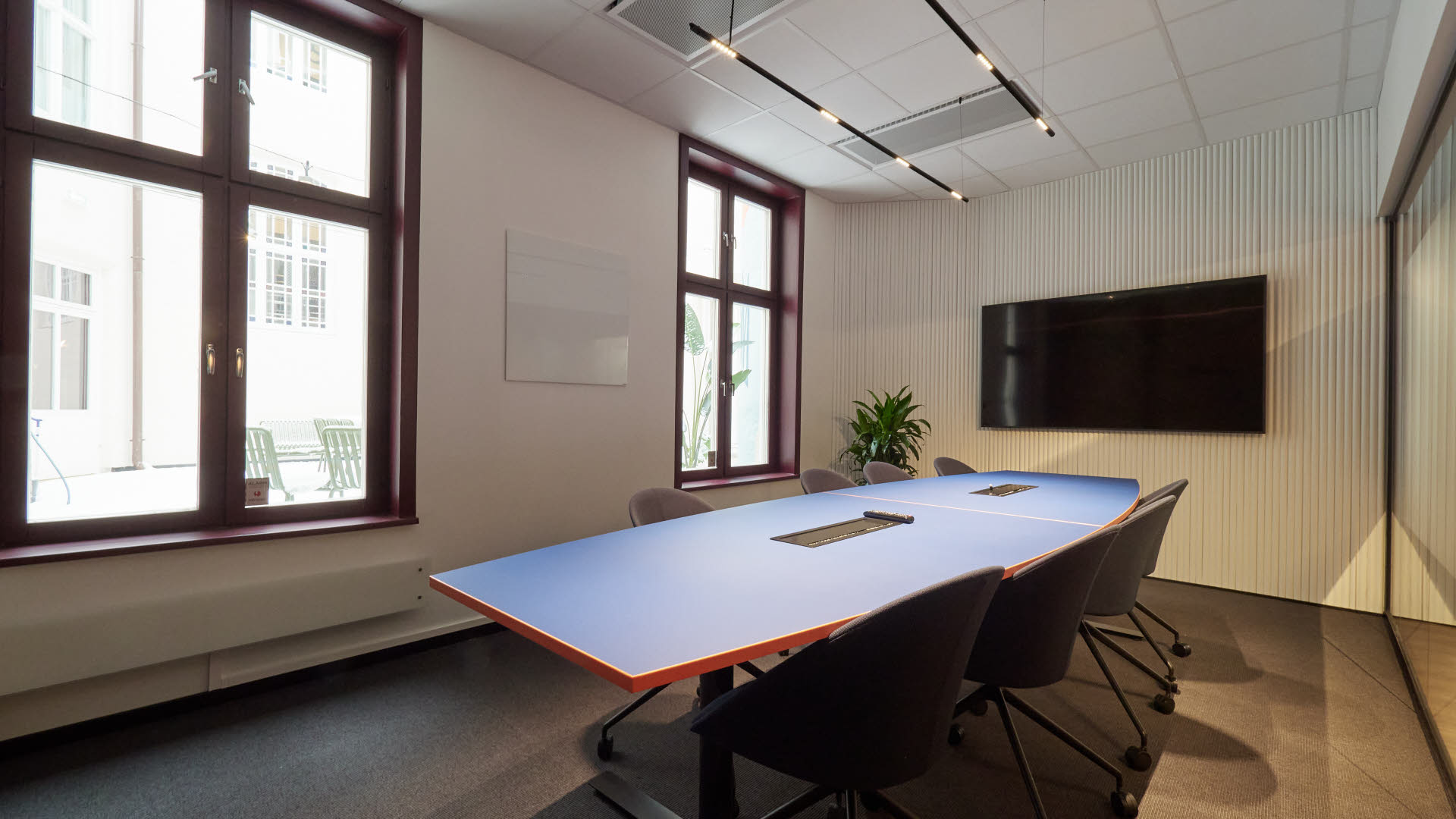 Bilde av et av møterommene i lokalene til Thon Flex i Karl Johans gate 5. Stort møterom med hvite vegger. blått bord,  sorte stoler og en stor TV på veggen.