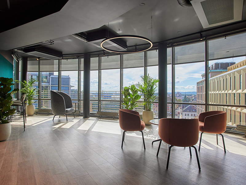 Bildet viser kontorfellesskapet Thon Flex i Stenersgata 2. En sittegruppe med tre røde stoler står i forkant av store vindusflater. Flott utsikt over Jernbanetorget, midt i Oslo sentrum.