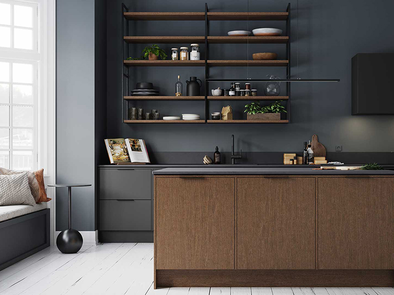 Bildet viser et kjøkken fra Norema. Kjøkkenfrontene er i mørkebrun med svart benkeplate. Veggen bak er malt i en mørk farge med en hylle i samme brunfarge som kjøkkenfronten.