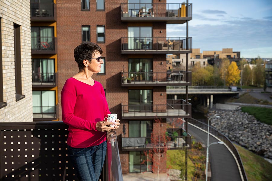 Bildet viser en dame i rød genser som står på balkongen sin i boligprosjektet Strømmen Verksted.