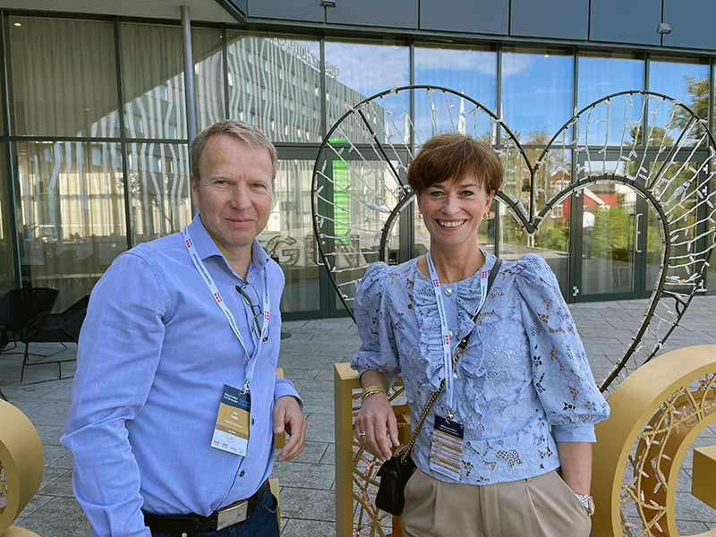 Mann og kvinne står foran bygning med glassfasade. Foto.