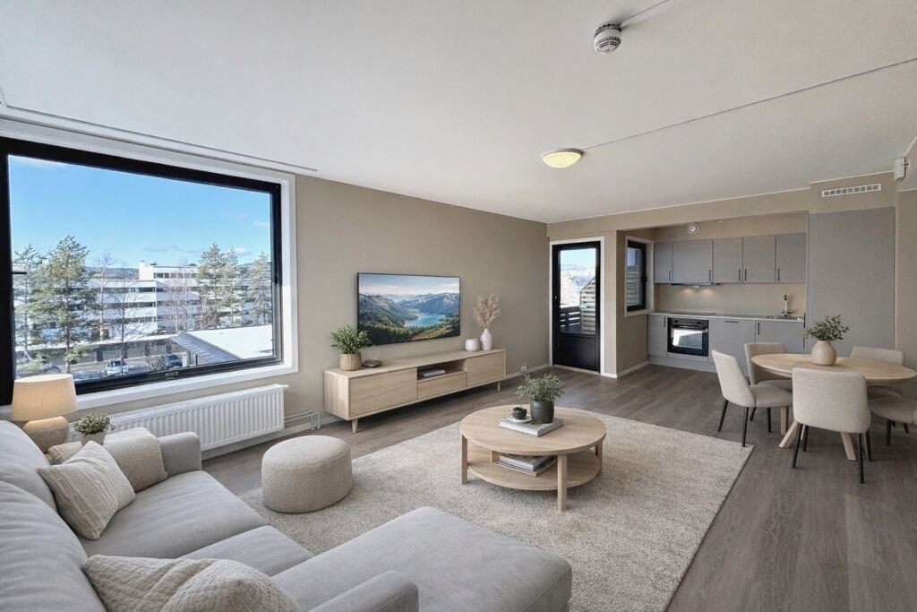 Lys og moderne stue med åpen kjøkkenløsning og store vinduer som slipper inn rikelig med dagslys. Her er det god plass til både hverdag og samvær. Bildet er innredet med KI.